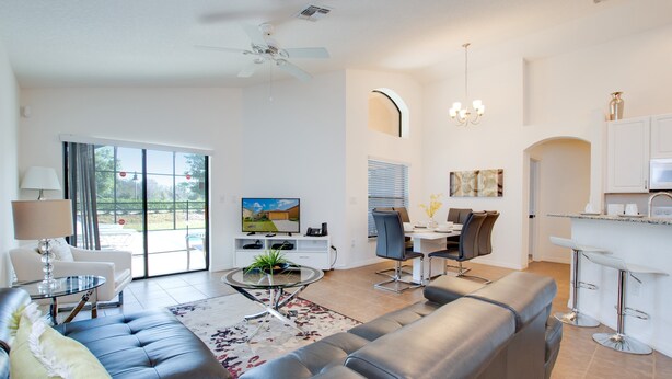 A modern living room with a grey sofa, a dining area with a table and chairs, a kitchen with a bar, and a large window with a view. - 2521rose (Davenport)