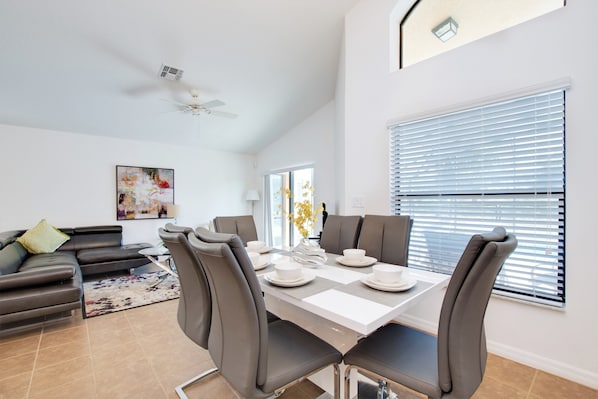 A modern dining area with a white table set for four, surrounded by grey upholstered chairs.