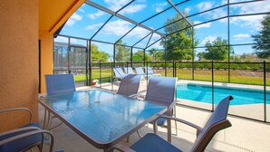 A covered outdoor area with a glass table and chairs, a pool, and a view of the surrounding landscape. - 2521rose (Davenport)