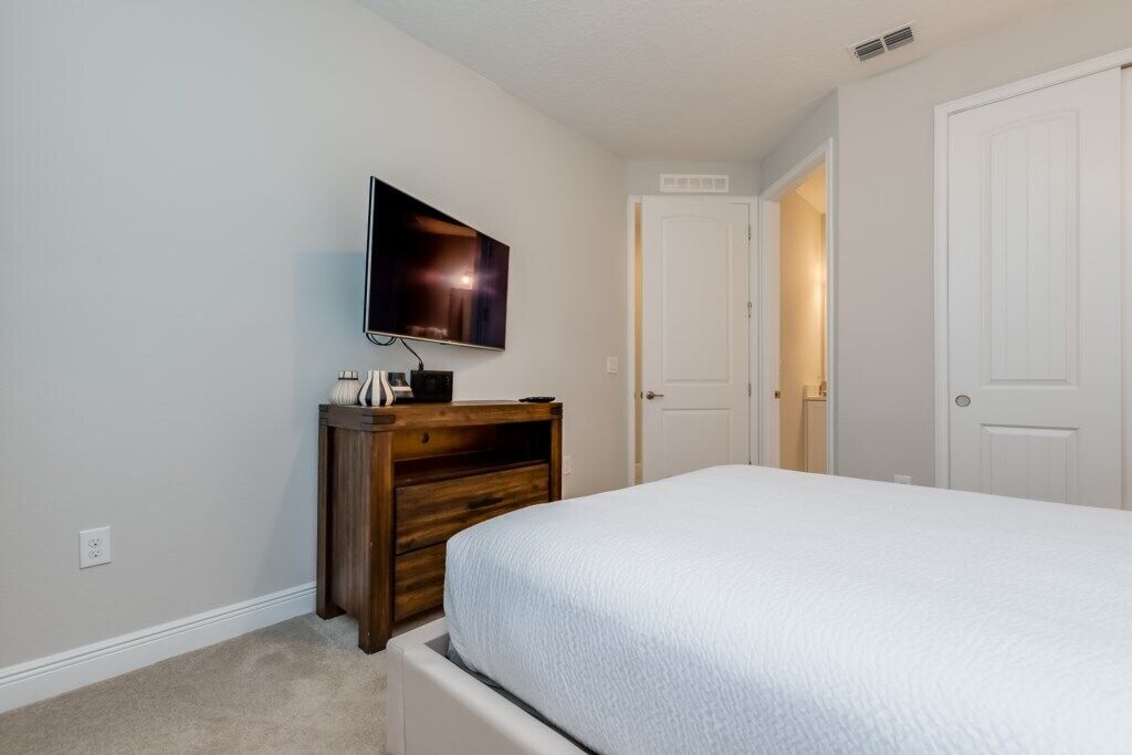 Une chambre à coucher avec un lit, un téléviseur posé sur un meuble en bois et une porte blanche.