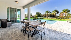 An outdoor patio with a pool, a table with chairs, and a wicker chair. - Encore Resort Villa W Private Pool and Spa 7670 (Kissimmee)