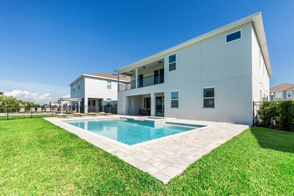 A modern two-story house with a swimming pool, a covered patio, and a well-maintained lawn.