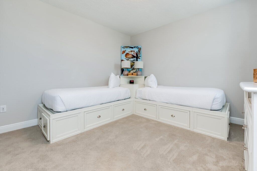 A bedroom with two single beds, a nightstand with a lamp, and a small shelf with decorative items.