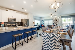 A modern kitchen with white cabinets, a central island with stools, and a dining area with a chandelier.