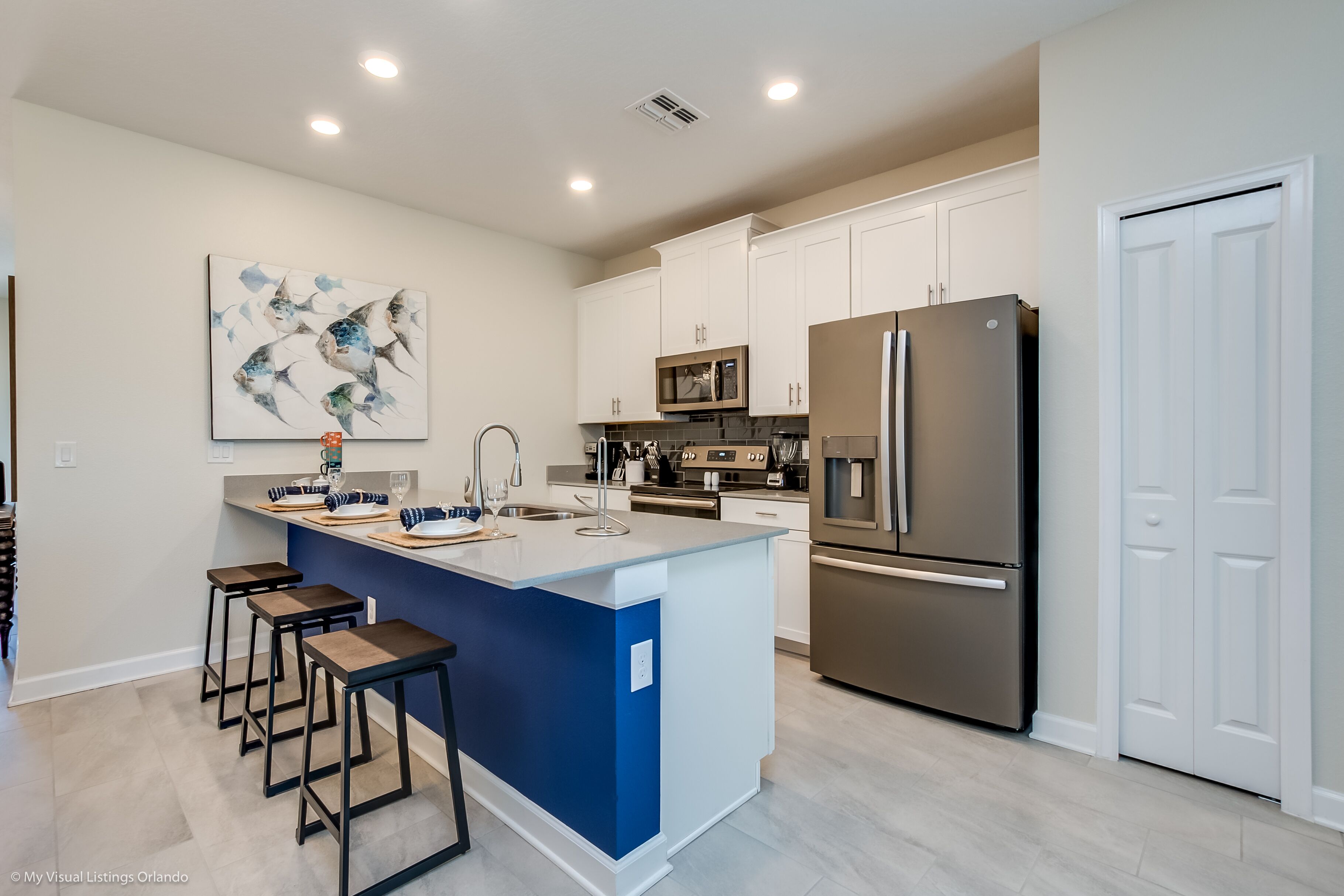 A modern kitchen with a central island, white cabinets, stainless steel appliances, and a blue accent wall.