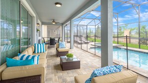 A covered patio area with outdoor seating, a pool, and a view of the backyard.