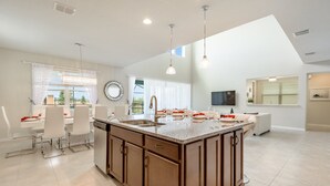 A spacious kitchen with a large island, white cabinetry, and pendant lighting.