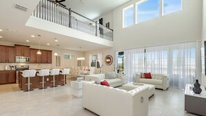 A spacious living area with a high ceiling, a kitchen with wooden cabinets, a dining area, and a balcony with a railing.