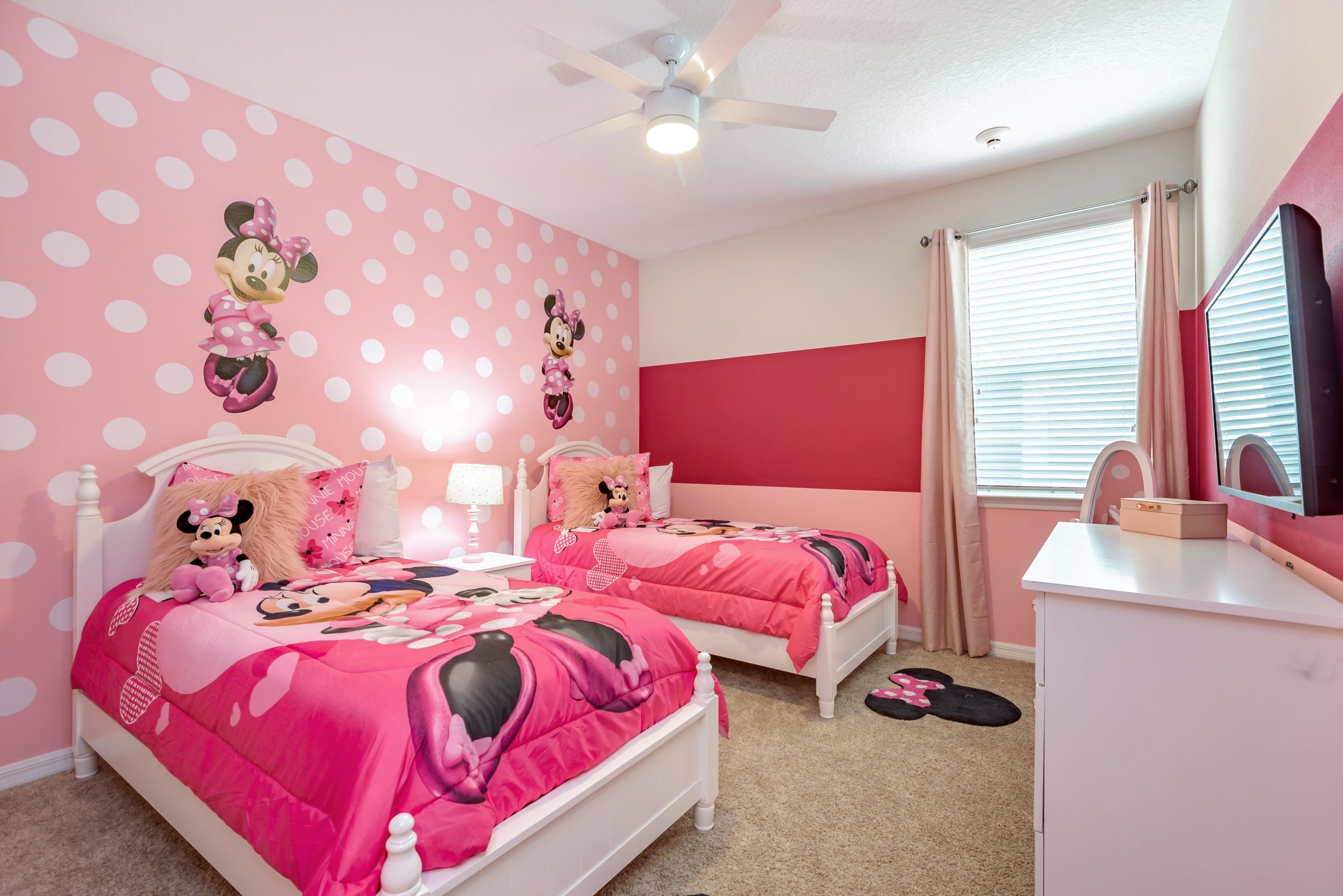 A pink-themed bedroom with two beds, a ceiling fan, and a dresser.