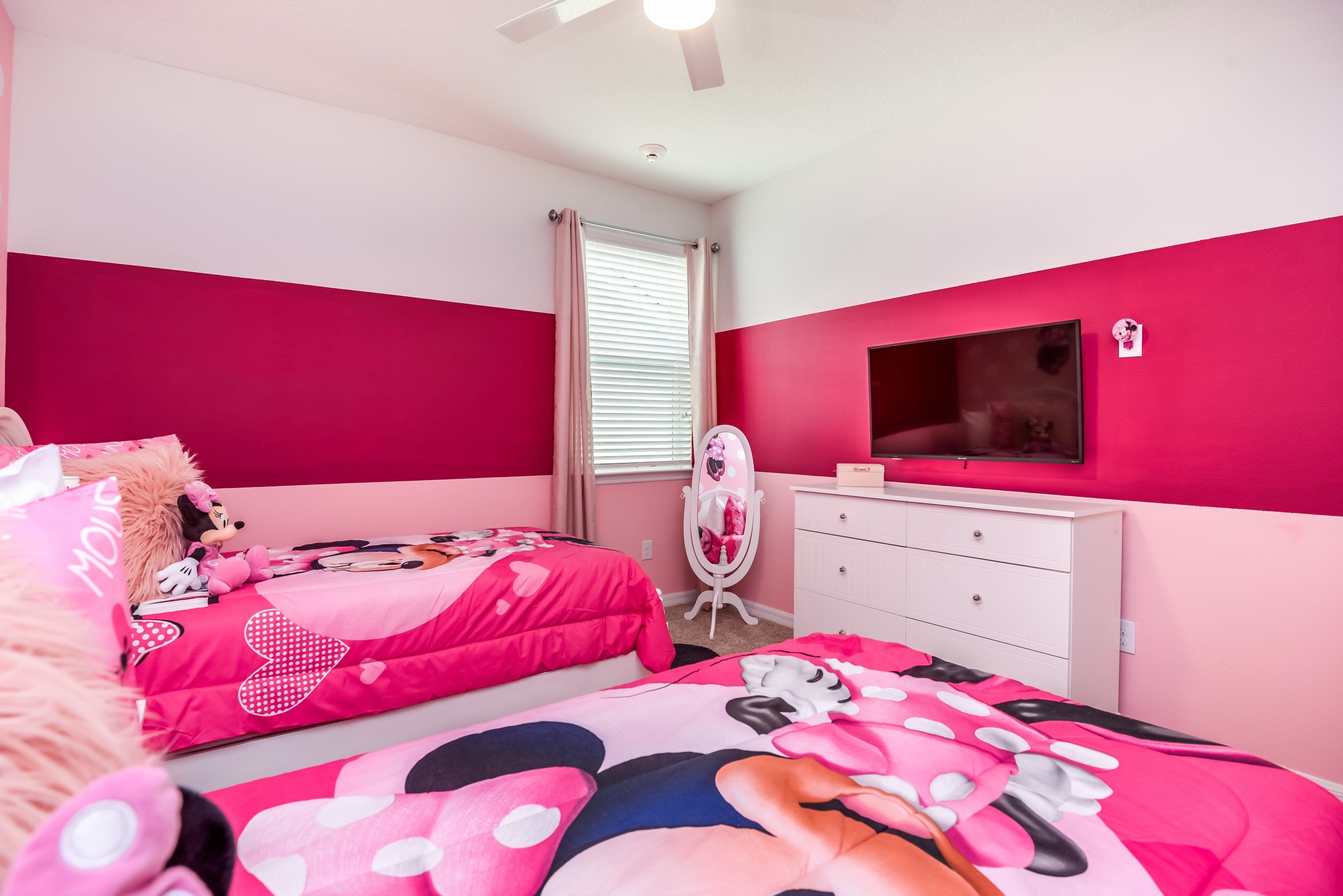 A pink-themed bedroom with two beds, a vanity, and a TV on the wall.