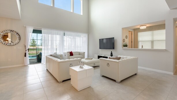 A spacious living room with a high ceiling, white sofas, a coffee table, and a TV mounted on the wall.