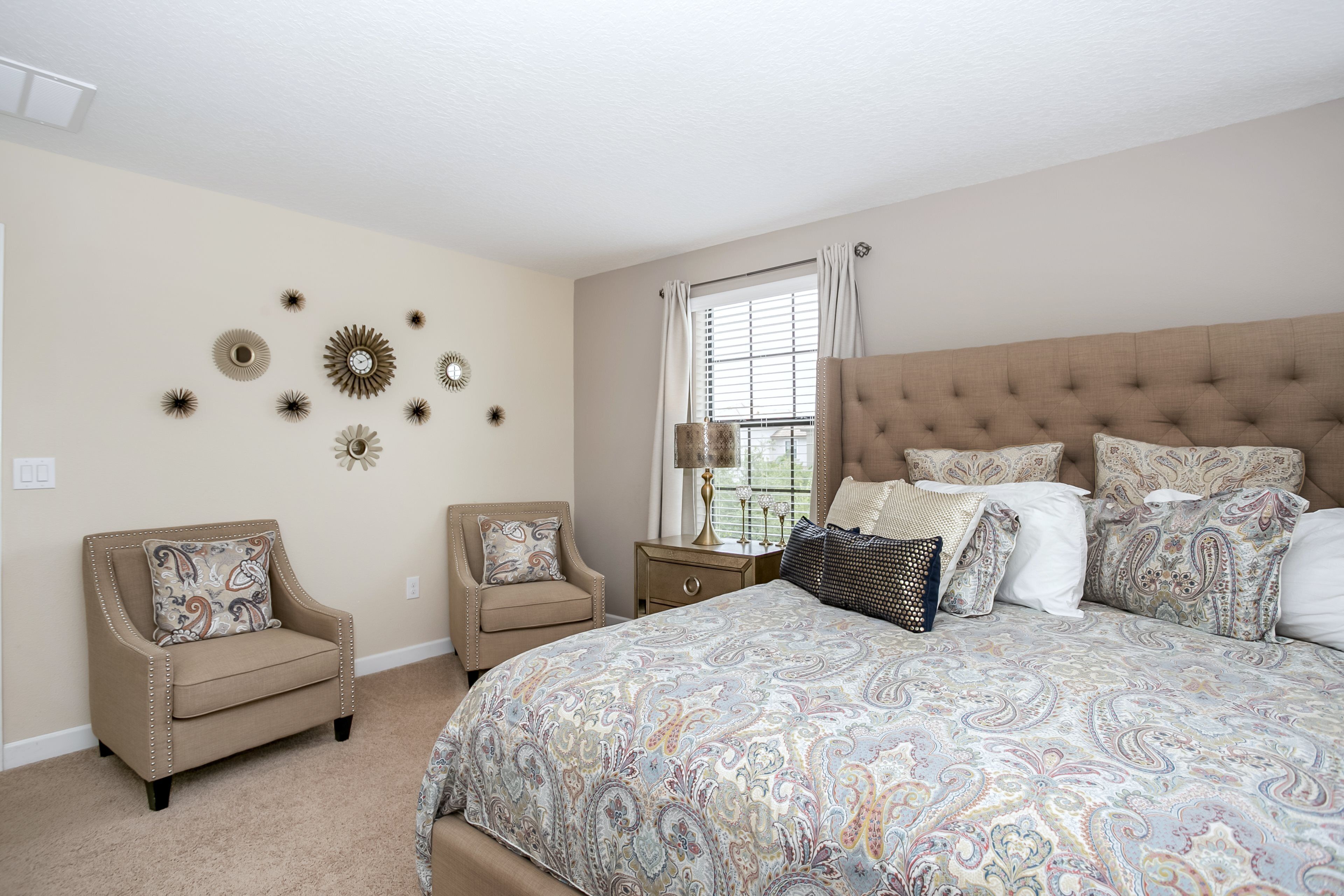 A bedroom with a large bed, two armchairs, a nightstand, and wall decor.