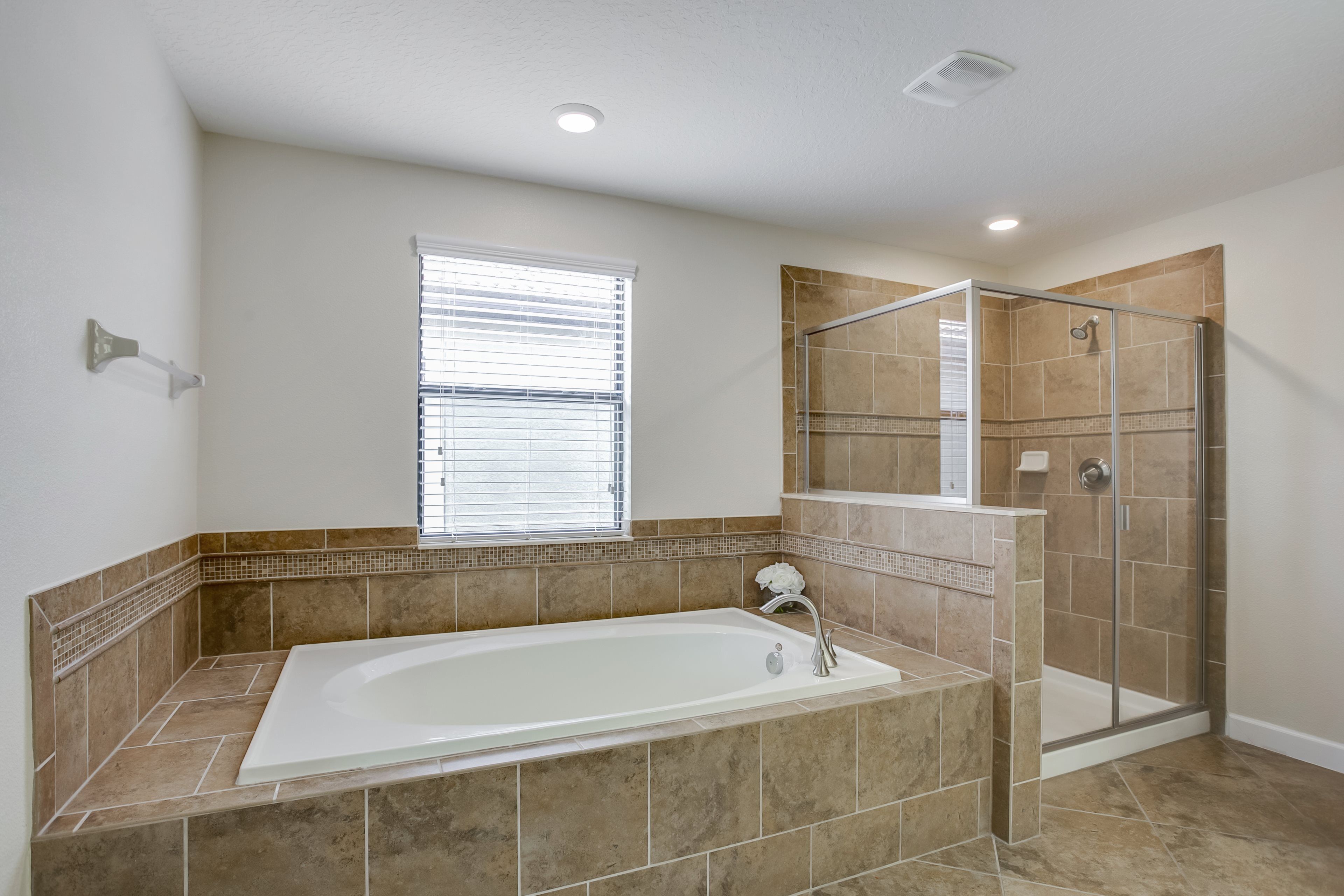 A bathroom with a bathtub, shower, and a window with blinds.
