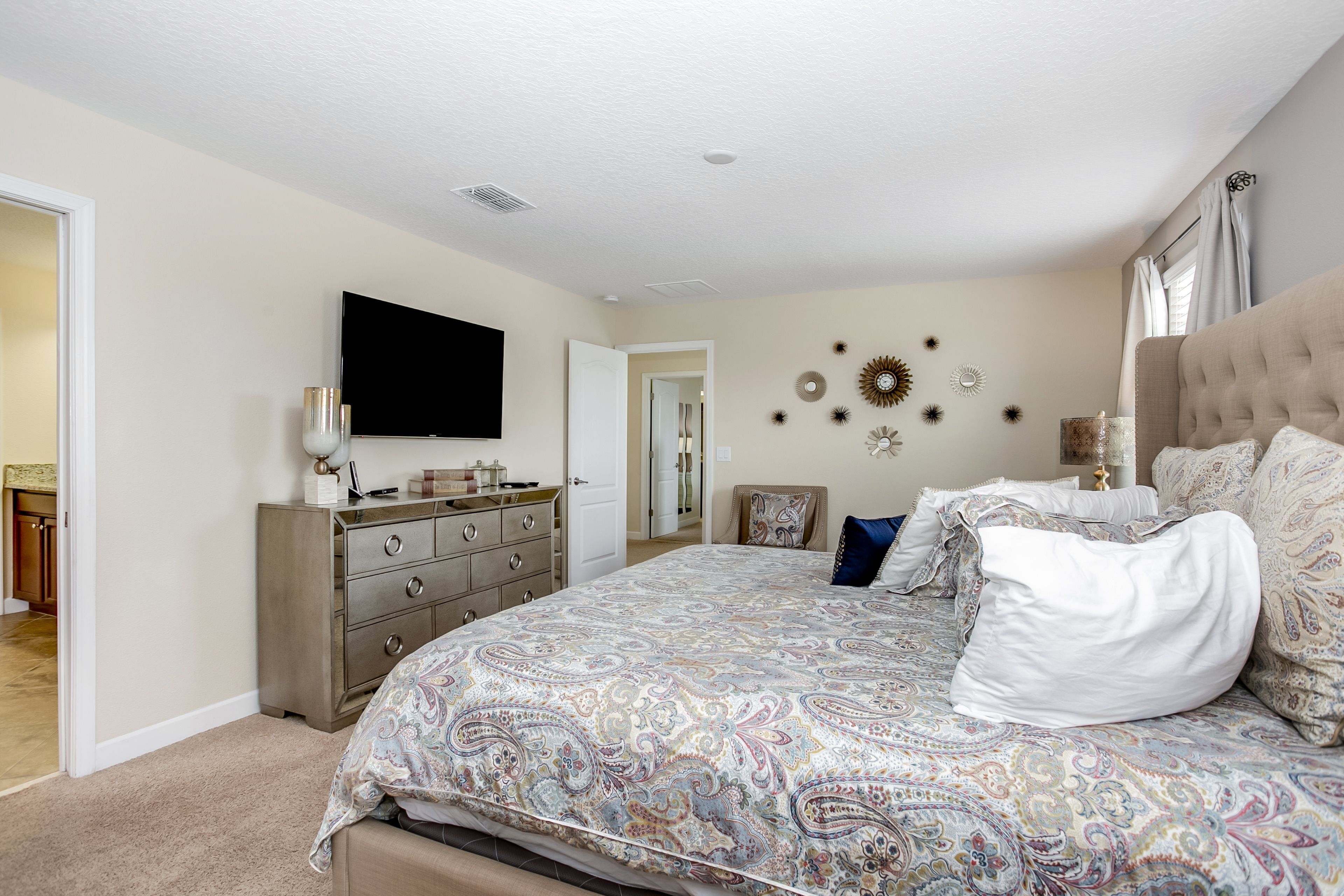 A bedroom with a large bed, a dresser, a television, and decorative wall art.