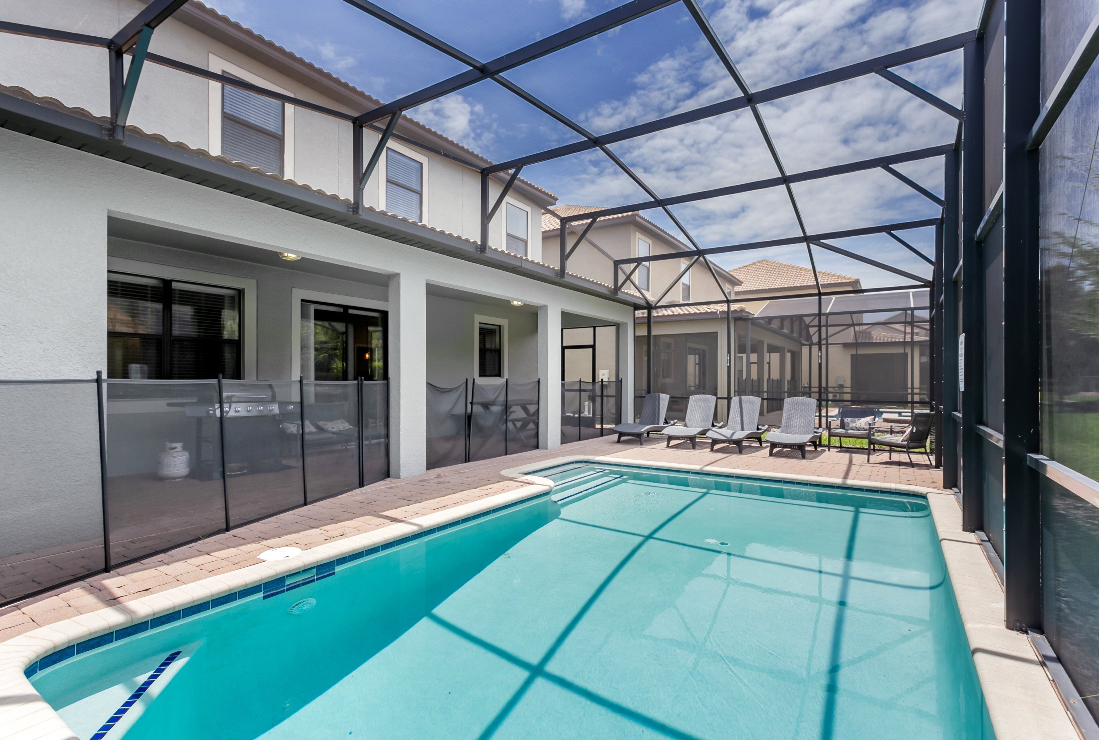 Ein Schwimmbecken mit klarem, blauem Wasser, umgeben von einer überdachten Terrasse mit Stühlen und einem Grill.