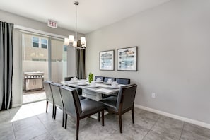 Un coin repas avec une table dressée pour quatre personnes, un lustre et une vue sur un patio équipé d’un barbecue.