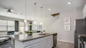 Une cuisine moderne avec des meubles blancs, des plans de travail en granit, un réfrigérateur en acier inoxydable et des luminaires suspendus.