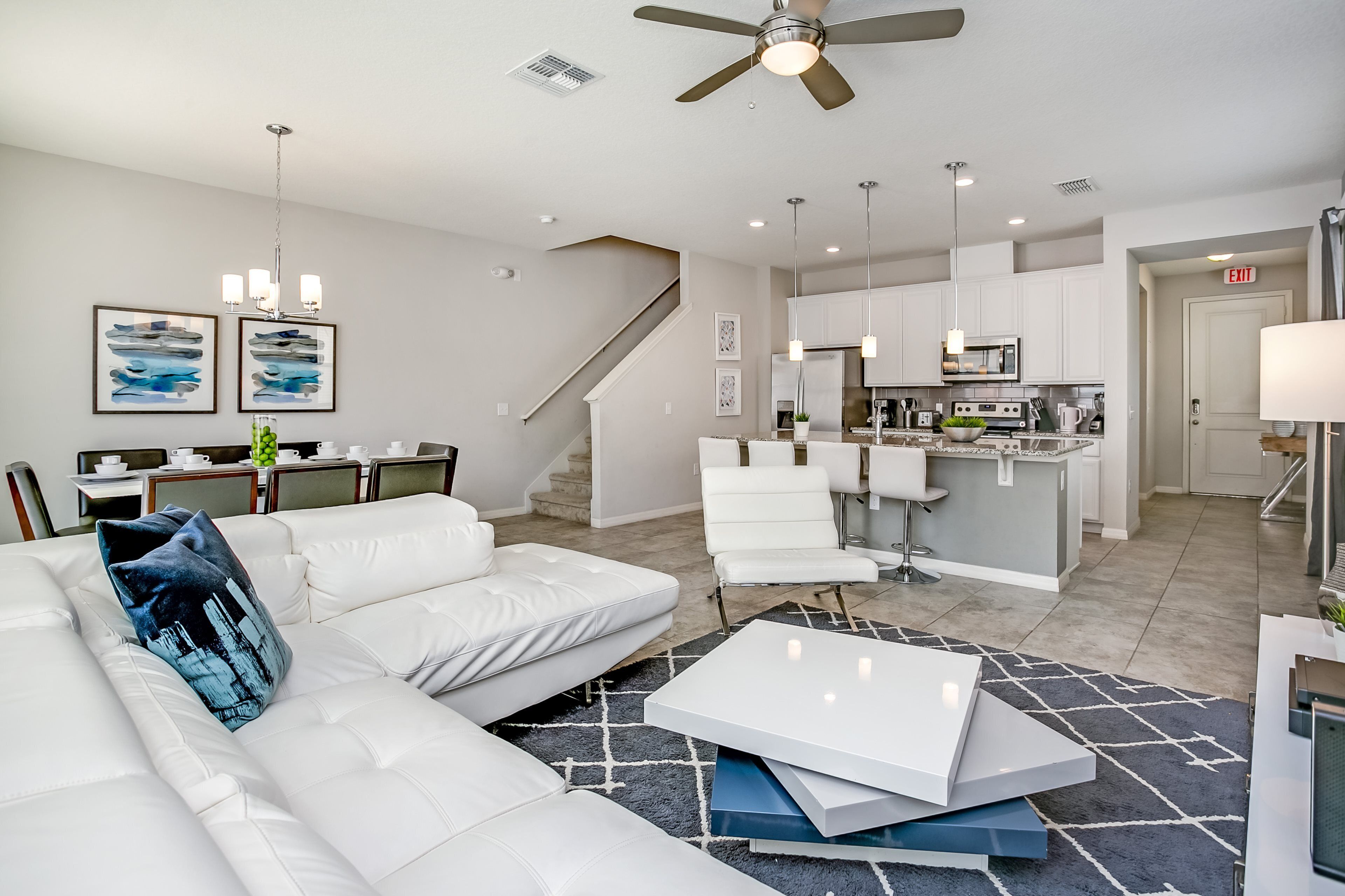A modern living room with a white sofa, a coffee table, and a staircase leading to the kitchen.