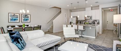A modern living room with a white sofa, a coffee table, and a staircase leading to the kitchen.