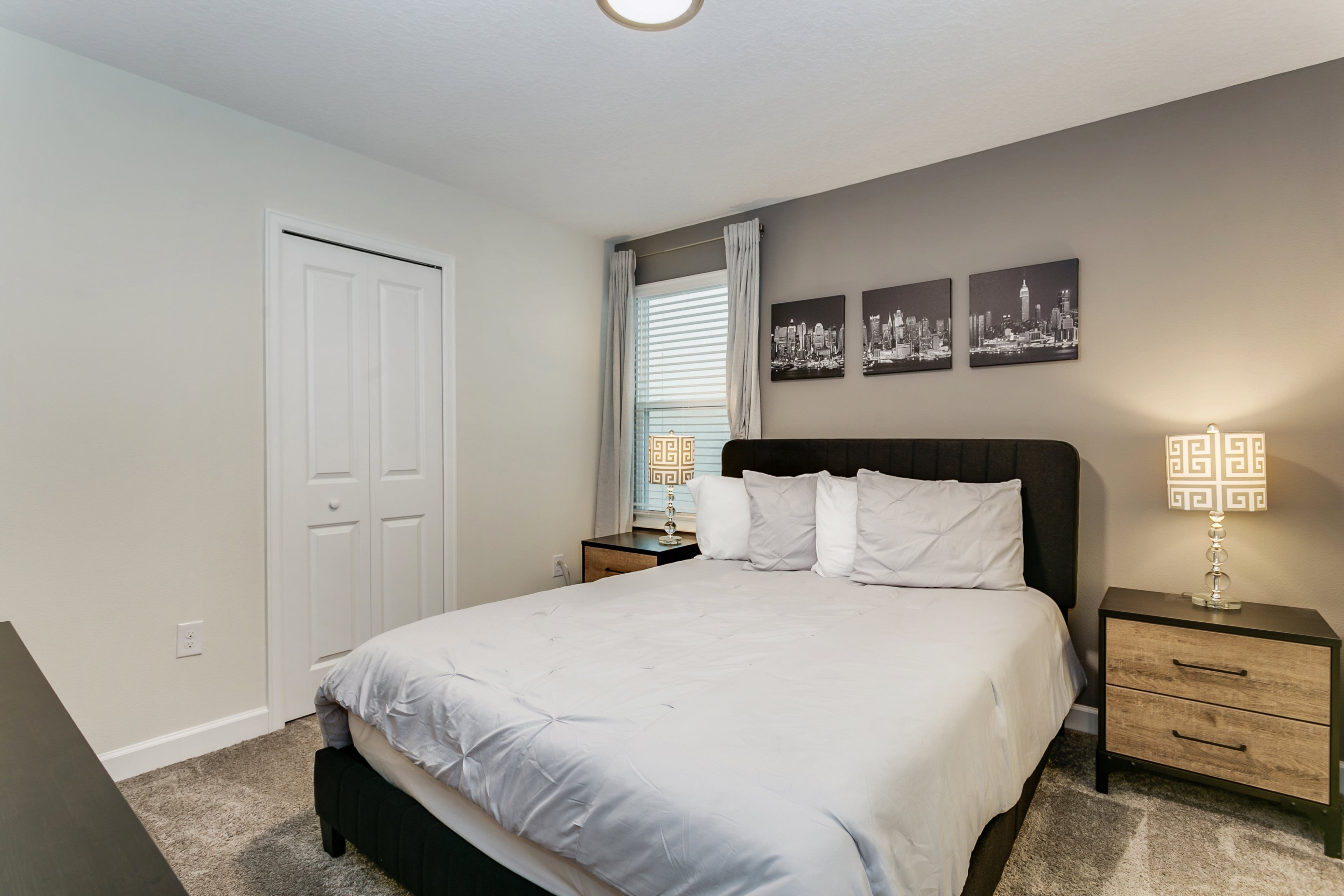 A bedroom with a bed, a nightstand, a lamp, a window with blinds, and a door.