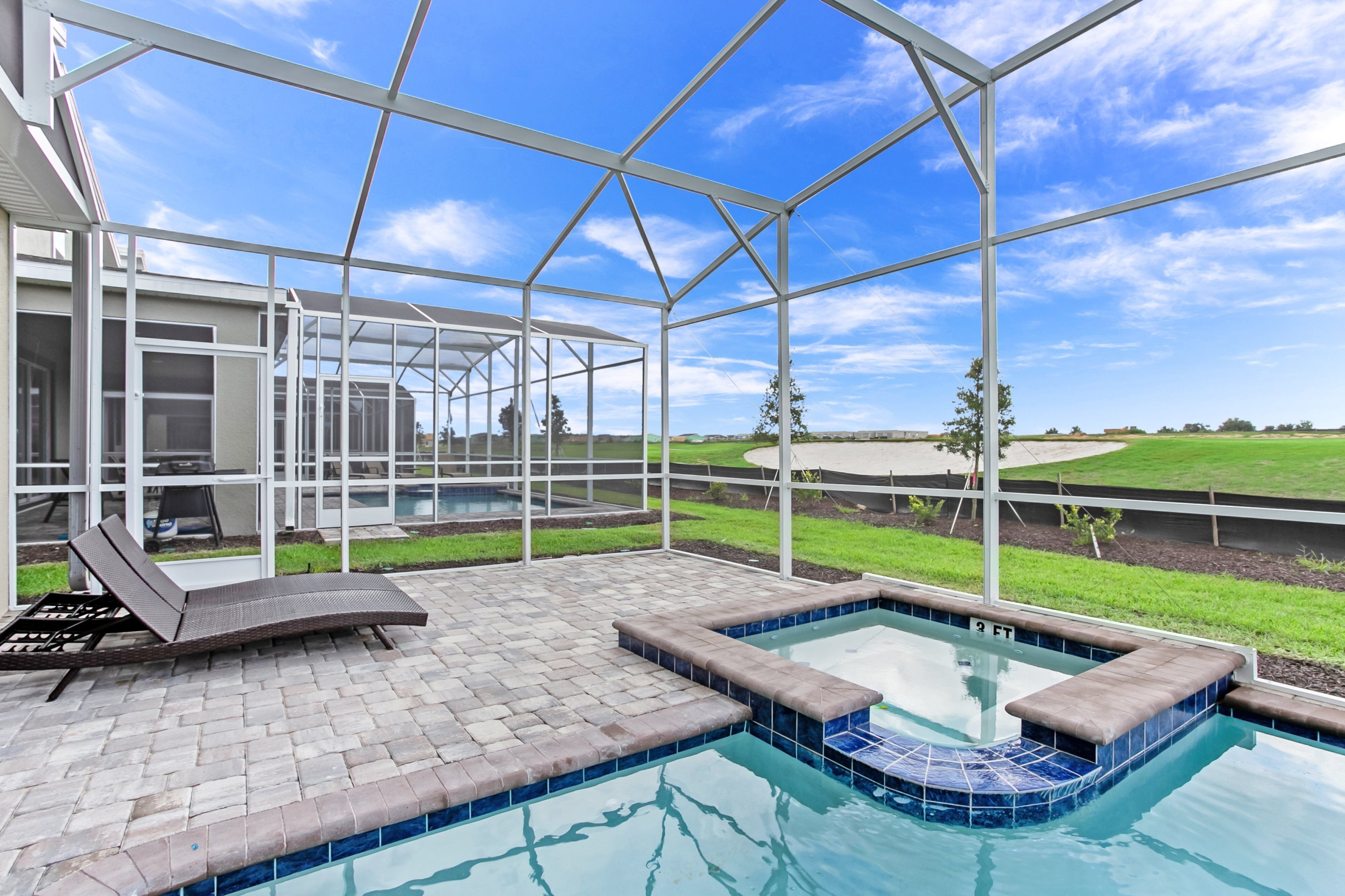 A covered outdoor swimming pool with a glass ceiling, a lounge chair, and a view of the surrounding landscape.