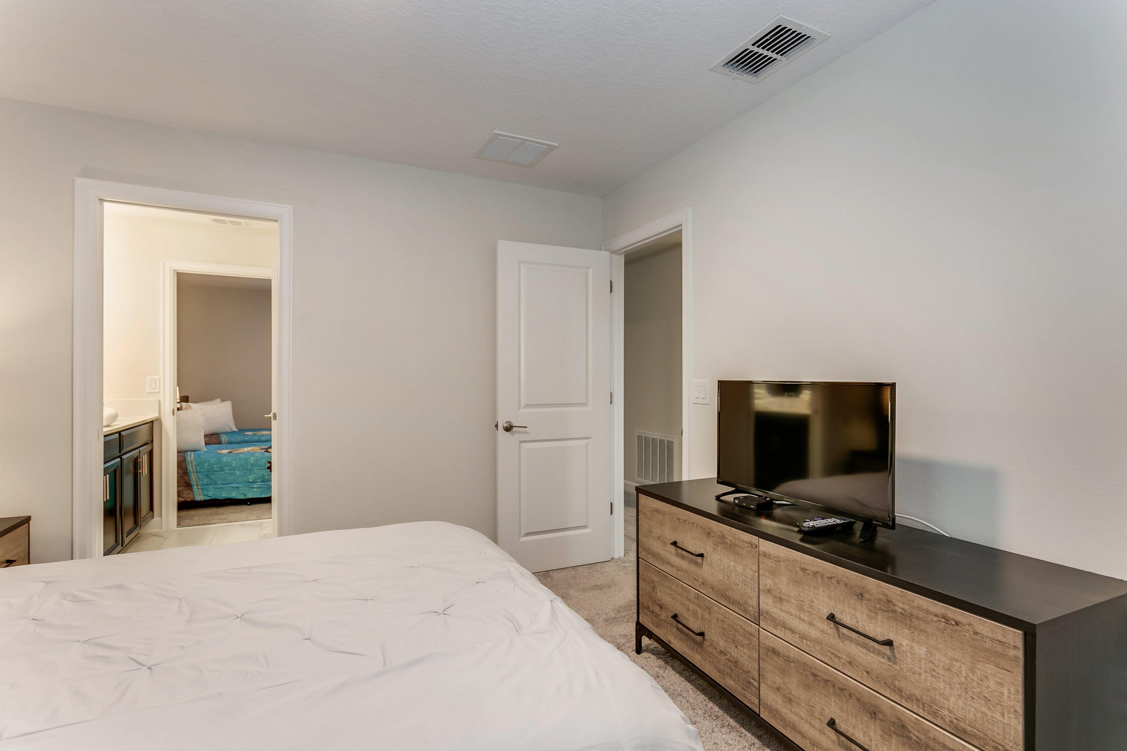 A bedroom with a bed, a dresser, a television, and a door leading to another room.