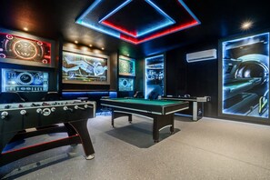 Une pièce équipée d’une table de billard, d’un baby-foot et de grands écrans numériques fixés aux murs.