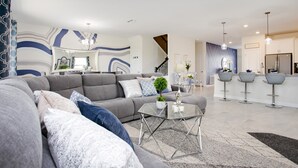 A modern living room with a grey sofa, a glass coffee table, and a staircase leading to an upper level. - 9 Bdrm Champions Gate Villa (Davenport)