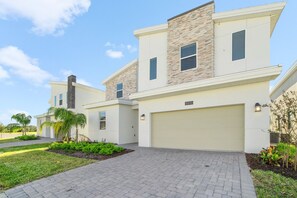 A modern two-story residential building with a garage, paved driveway, and landscaped garden.
