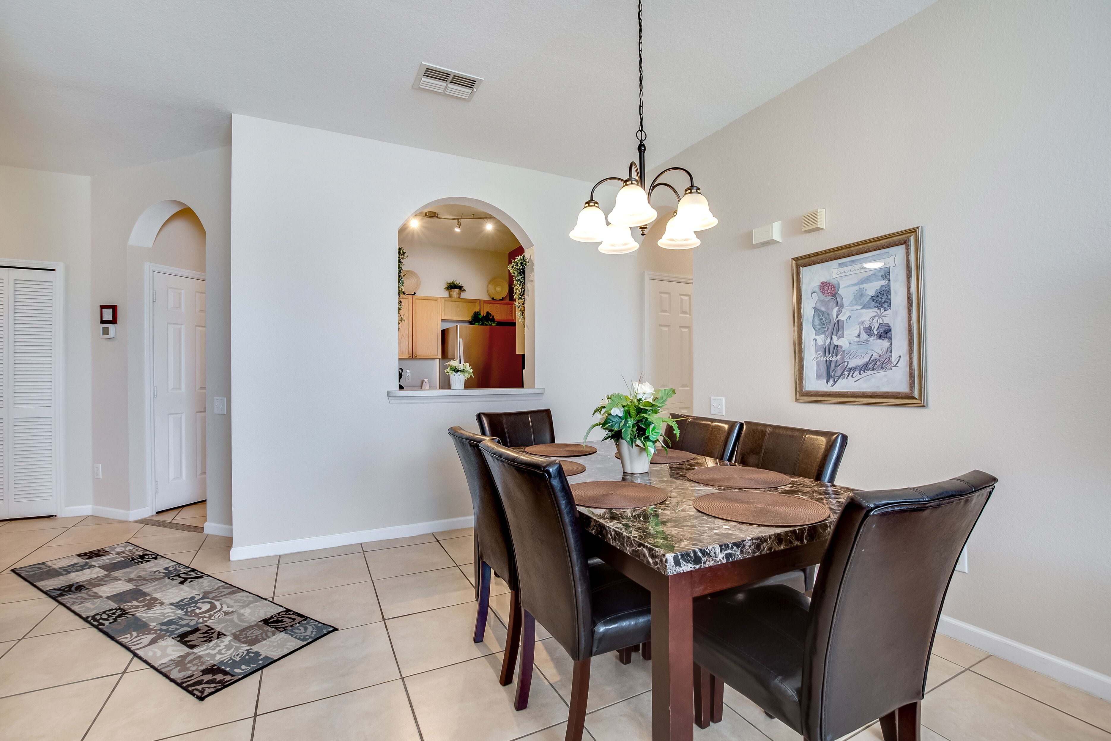 A dining area with a marble table, leather chairs, a hanging light fixture, and a framed picture on the wall.