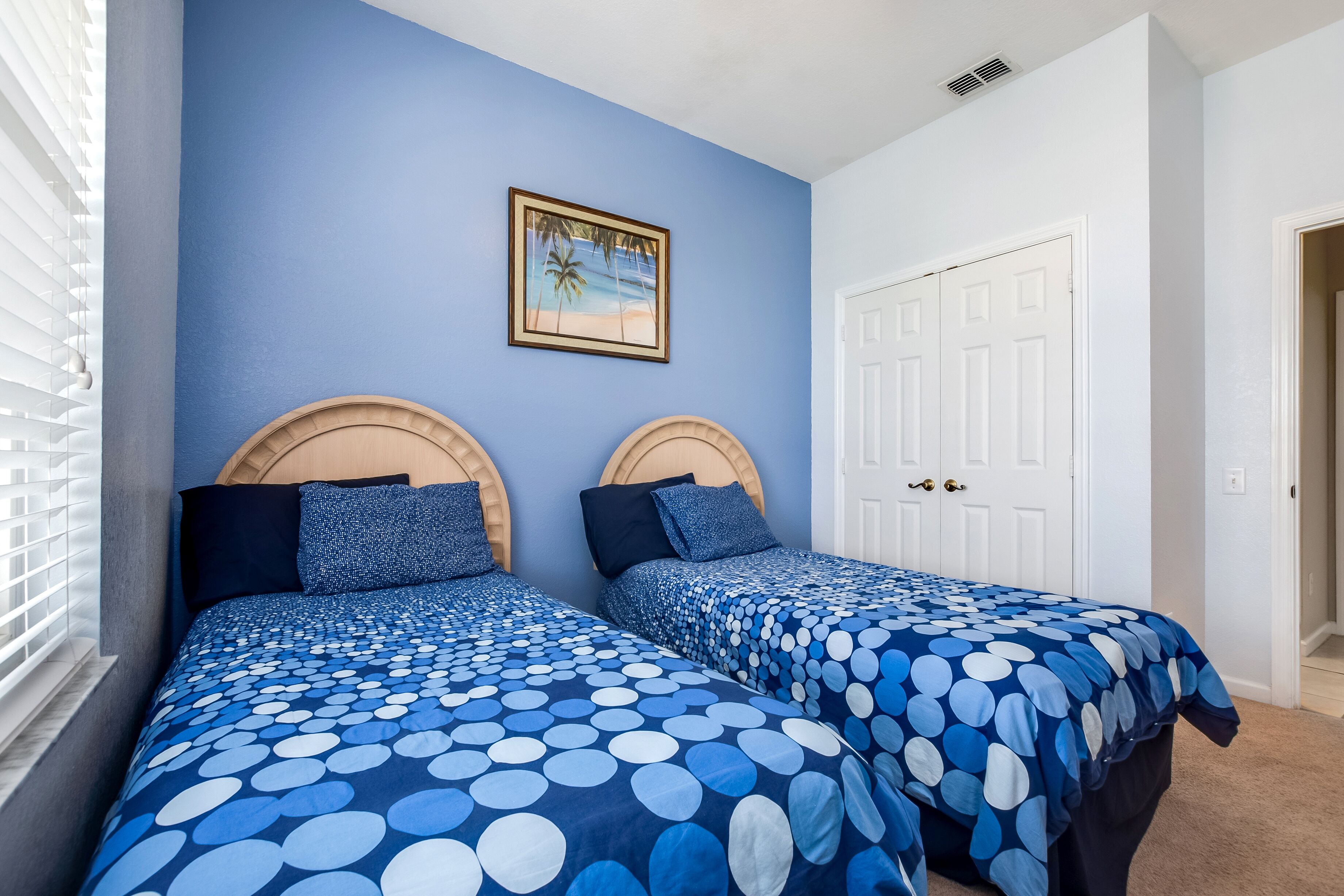 A bedroom with two beds, each with a headboard, a framed picture on the wall, and a white door.