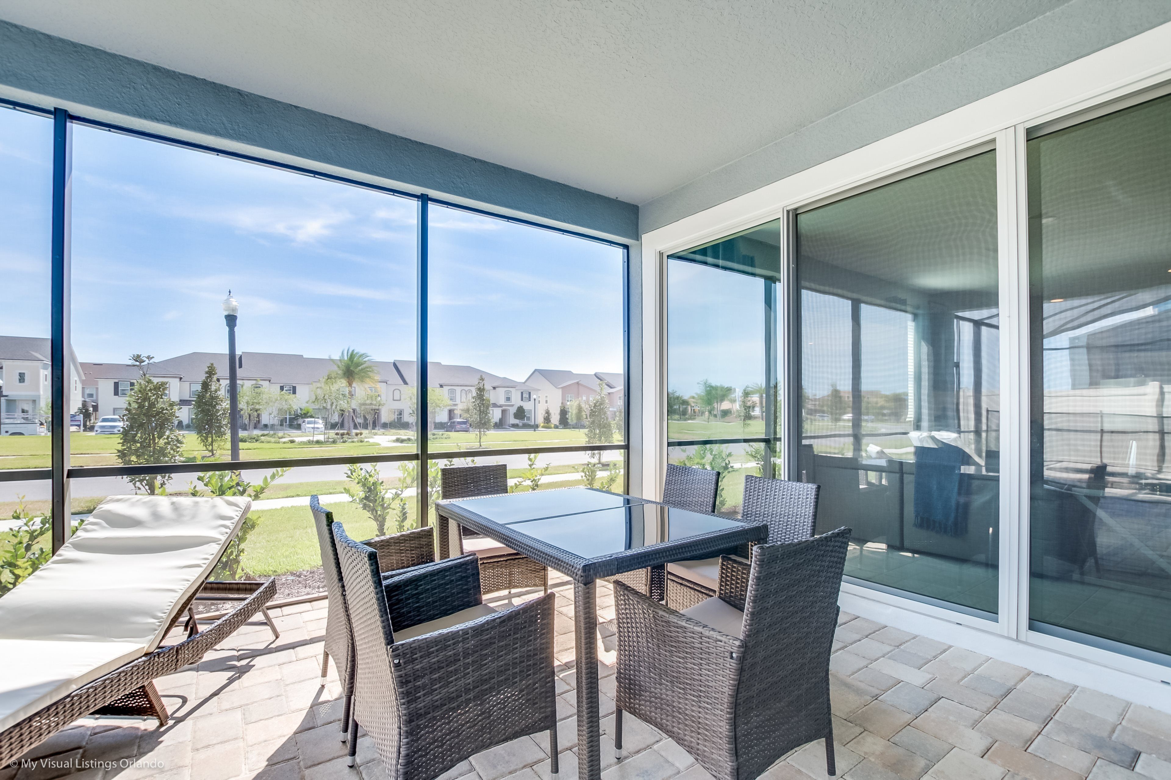 A balcony with wicker furniture, a glass table, and a view of a residential area.