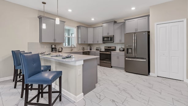 A modern kitchen with grey cabinets, stainless steel appliances, a marble floor, and a central island with bar stools. - Family Friendly! 6bed 5Ba Villa with Pool (Kissimmee)
