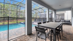 A covered patio with a pool, outdoor seating, and a view of the surrounding forest. - Family Friendly! 6bed 5Ba Villa with Pool (Kissimmee)