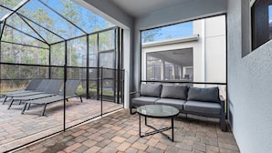 A modern patio area with a glass enclosure, a sofa, and a glass table. - Family Friendly! 6bed 5Ba Villa with Pool (Kissimmee)