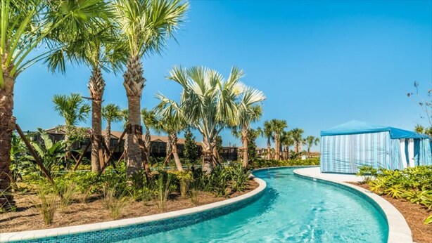 A swimming pool with a curved edge, surrounded by palm trees and a clear blue sky. - Lake View Villa (Kissimmee)