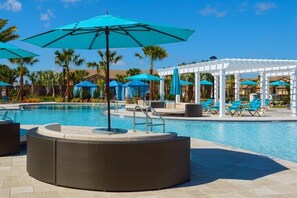 Uma área de piscina com espreguiçadeiras, guarda-sóis e um pergolado.