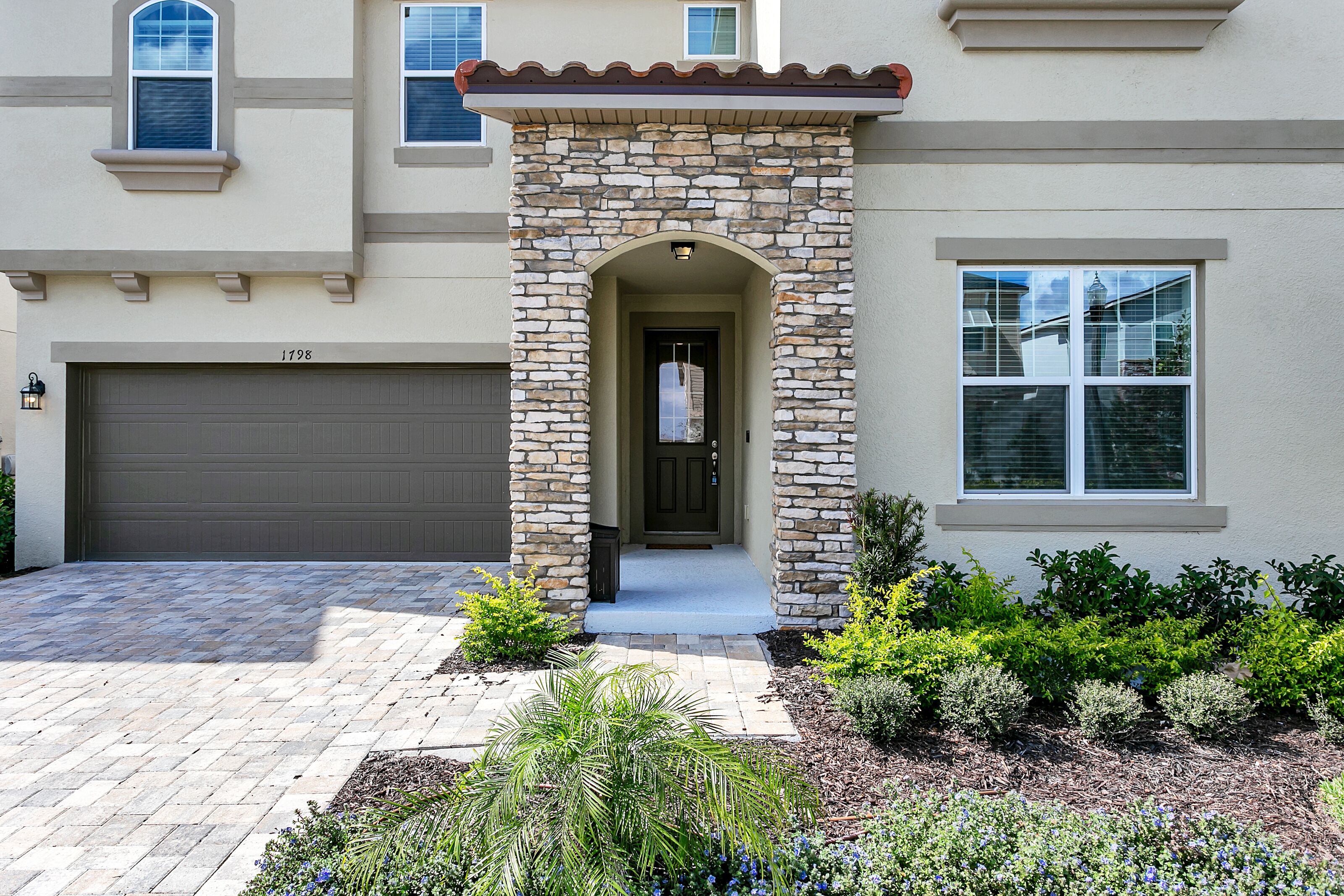 A house with a stone facade, a garage, and a well-maintained front yard with various plants.