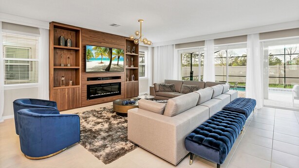 A modern living room with a large TV, a sofa, a blue chair, and a wooden entertainment unit. - 9 BD 6,5 BH Pool, Spa & Game Room (Kissimmee)