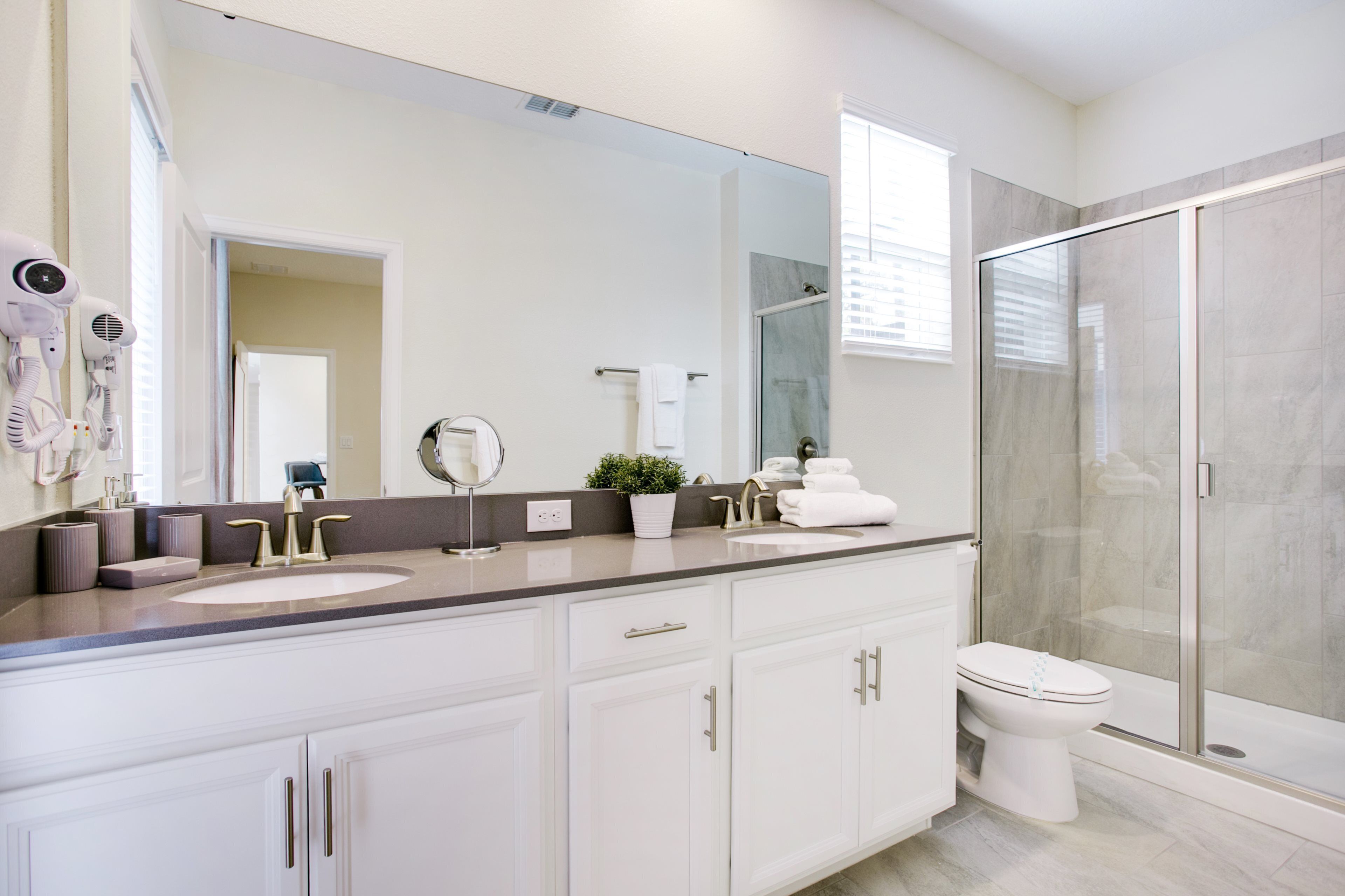 A modern bathroom with a large mirror, two sinks, a toilet, and a glass shower enclosure.