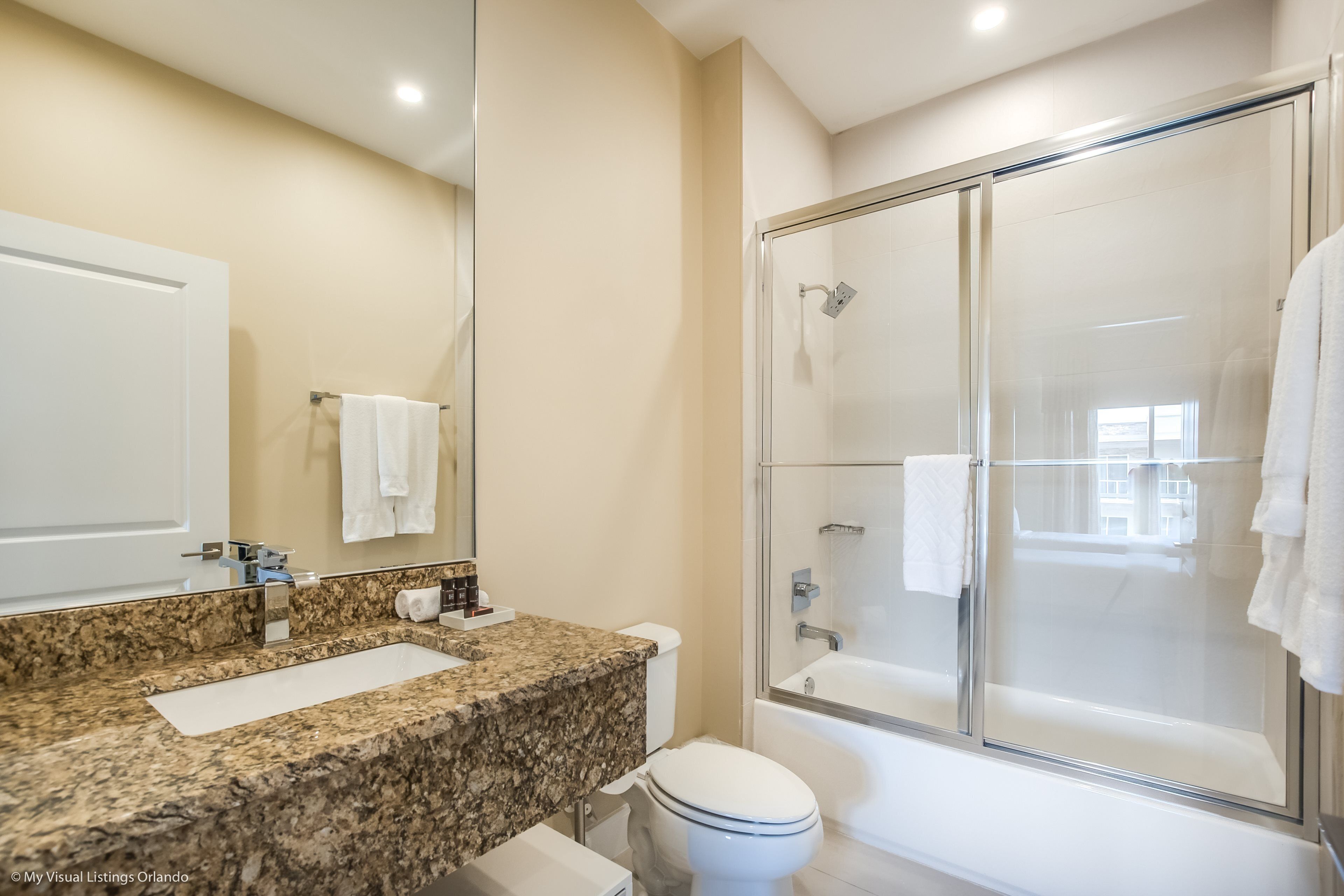Une salle de bain dotée d’un comptoir en granit, de toilettes, d’une douche à parois de verre et d’une baignoire.