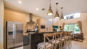 A modern kitchen with a stainless steel refrigerator, a built-in oven, and a large island with bar stools. - 3139brasillia (Kissimmee)