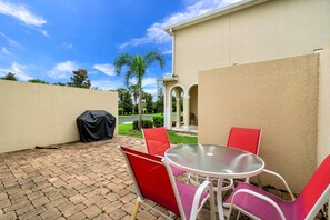 An outdoor patio with a table and chairs, a covered grill, and a view of a landscaped garden and palm trees. - 3193tocoa (Kissimmee)