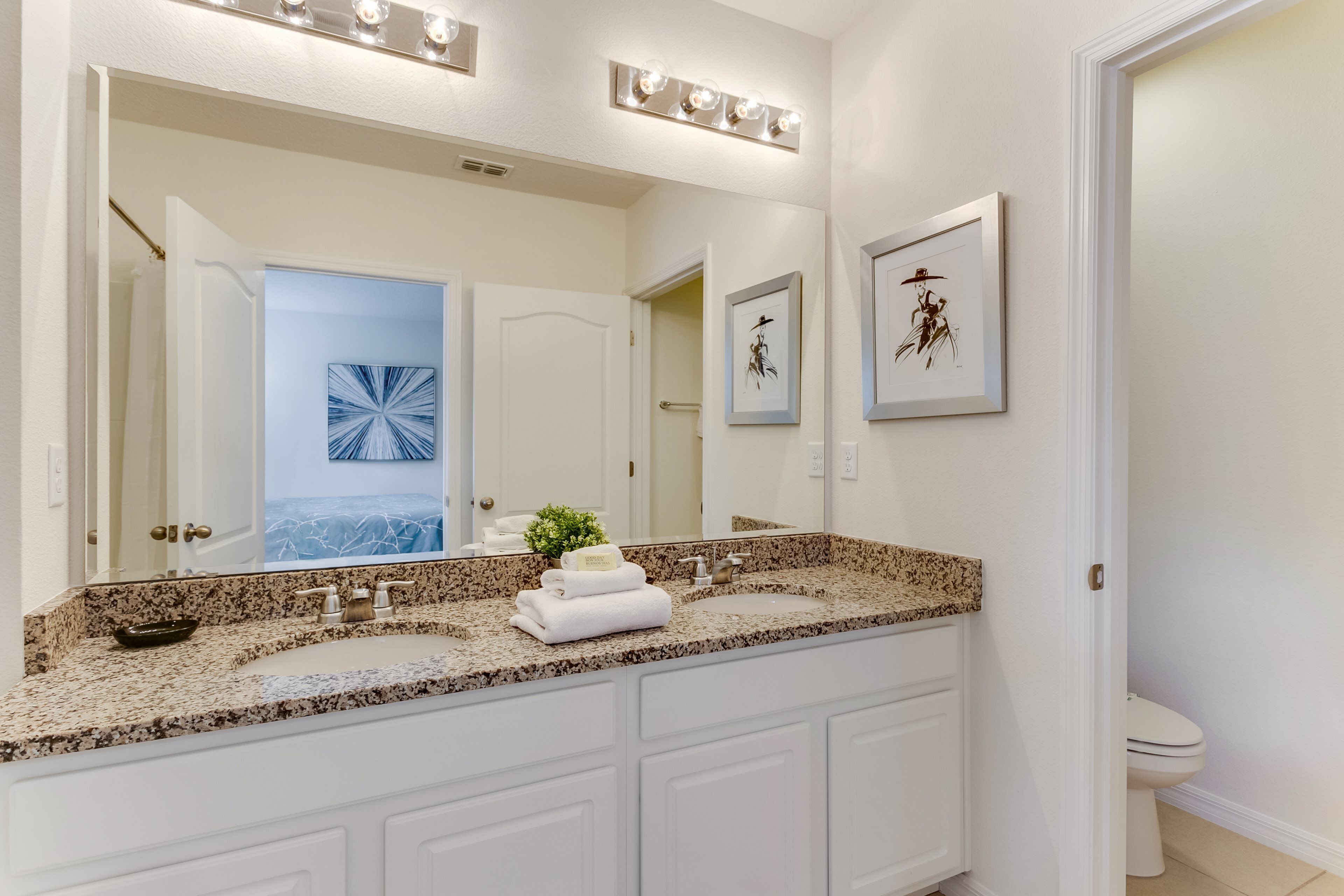A bathroom with a double sink vanity, a large mirror, and framed artwork on the wall.