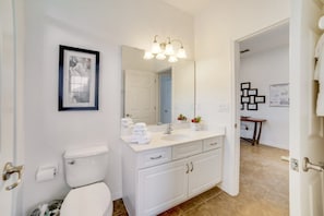 A modern bathroom with a white sink, mirror, and toilet. There is a framed picture on the wall and a small potted plant on the counter. - 2586rose (Davenport)