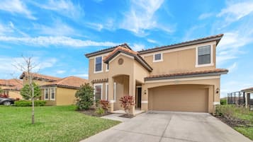 A two-story house with a beige exterior, a tiled roof, and a garage.