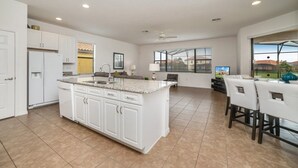 A spacious kitchen with white cabinetry, a large island, and a dining area with a table and chairs. - 2586rose (Davenport)
