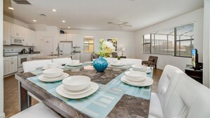A modern kitchen with white cabinets, a dining area with a marble table, and a large vase with flowers. - 2586rose (Davenport)