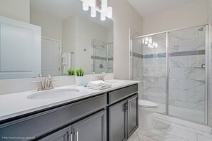 A modern bathroom with a double sink vanity, a glass shower enclosure, and a toilet.