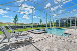 A covered outdoor swimming pool area with lounge chairs and a hot tub.